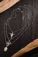 Multi-layered necklace with bull skull and cactus pendant on a dark wooden surface