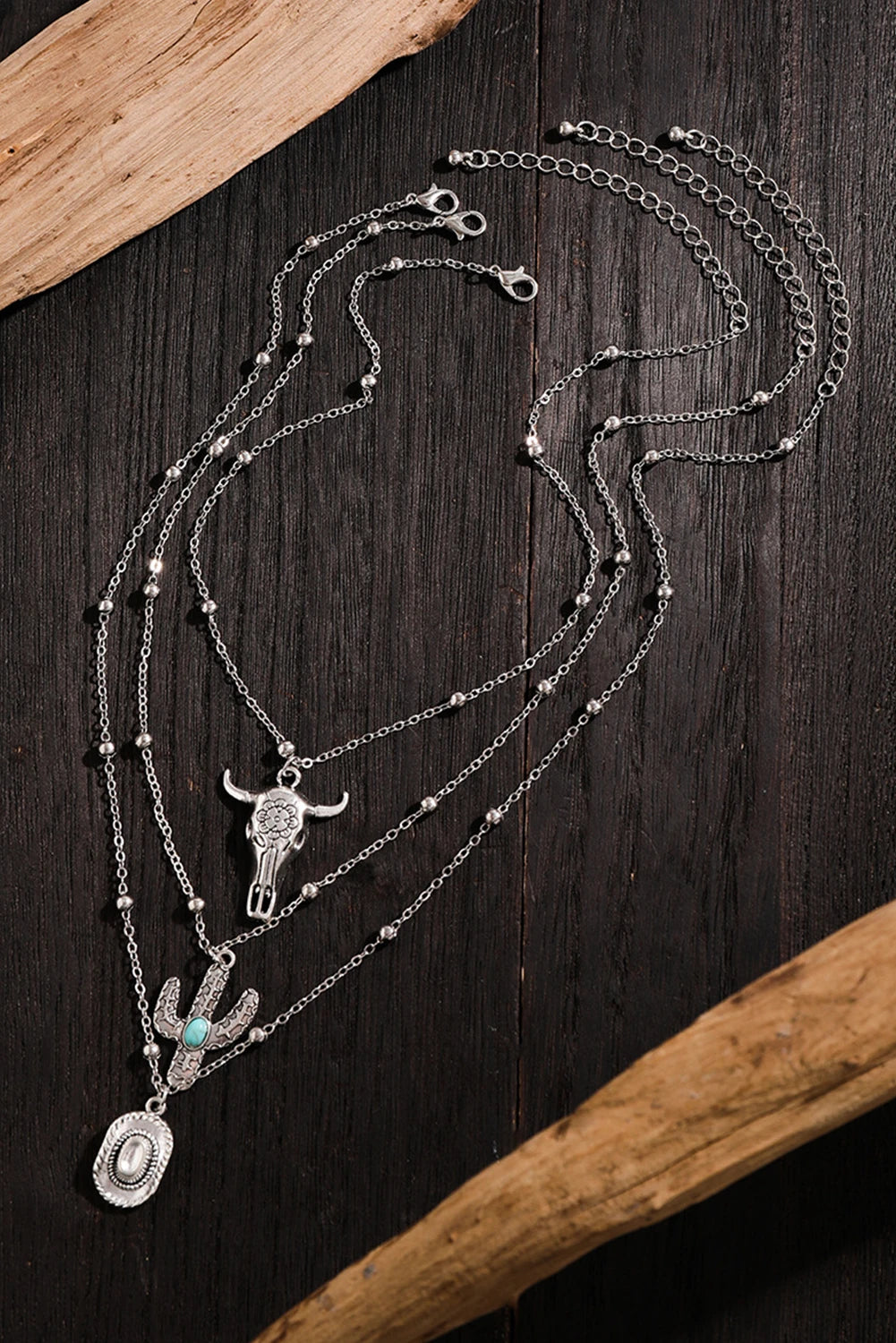 Multi-layered necklace with bull skull and cactus pendant on a dark wooden surface