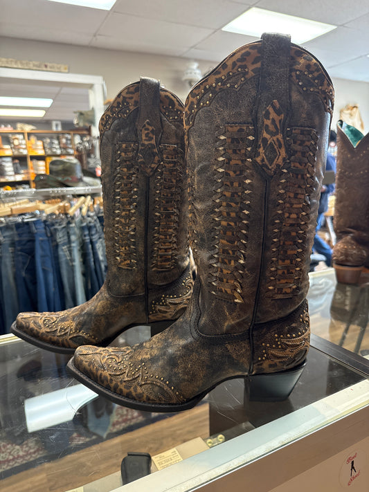Pair of worn cowboy boots with intricate designs on a glass surface.