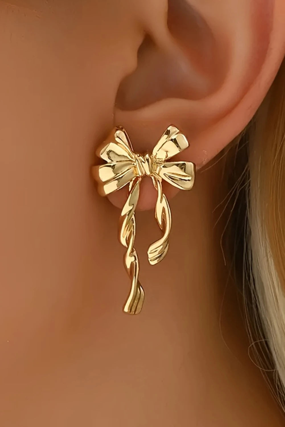 Gold bow-shaped earring worn on an ear with a neutral background