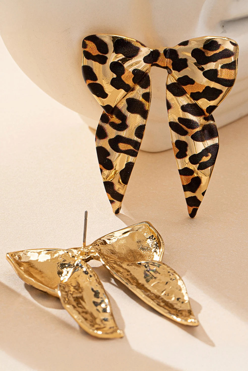 Gold butterfly-shaped earrings with leopard print design on a beige background