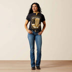 Woman wearing a black graphic t-shirt and blue jeans standing against a plain background