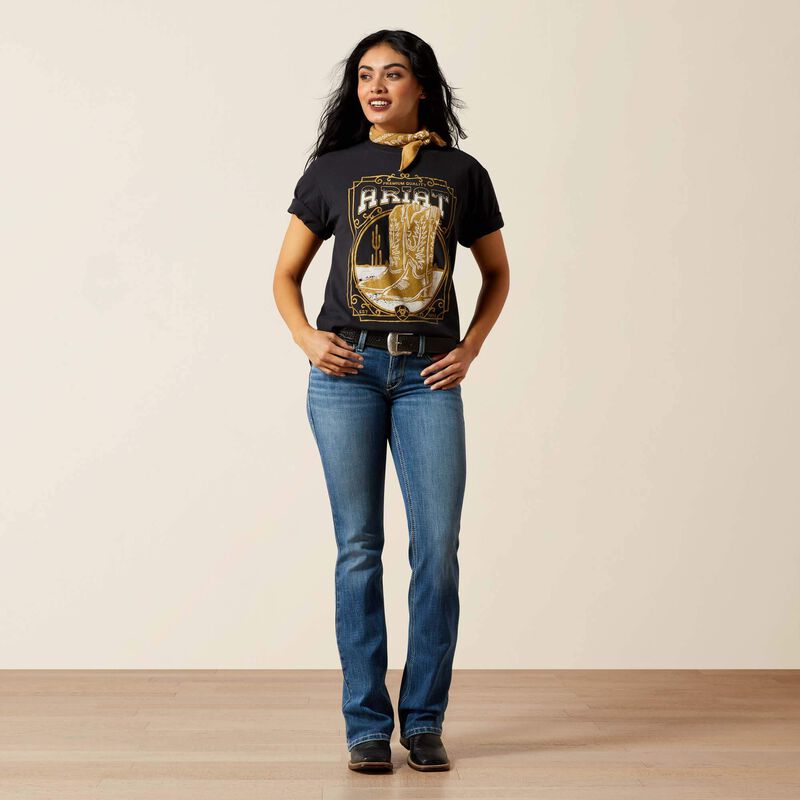 Woman wearing a black graphic t-shirt and blue jeans standing against a plain background