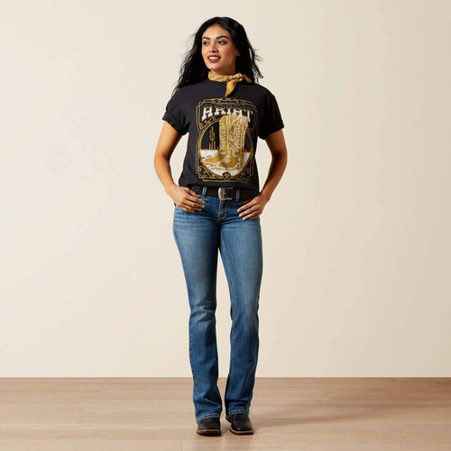 Woman wearing a black graphic t-shirt and blue jeans standing against a plain background
