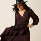 Woman wearing a dark brown dress and black hat against a beige background