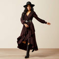 Woman wearing a long brown dress with a belt and black boots on a beige background
