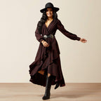 Woman wearing a long brown dress with a belt and black boots on a beige background