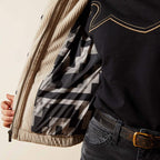 Close-up of a person wearing a beige jacket with a patterned lining, black shirt, and jeans.