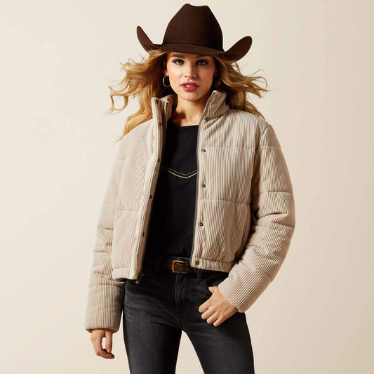 Woman wearing a beige puffer jacket, black top, dark jeans, and a brown cowboy hat on a beige background