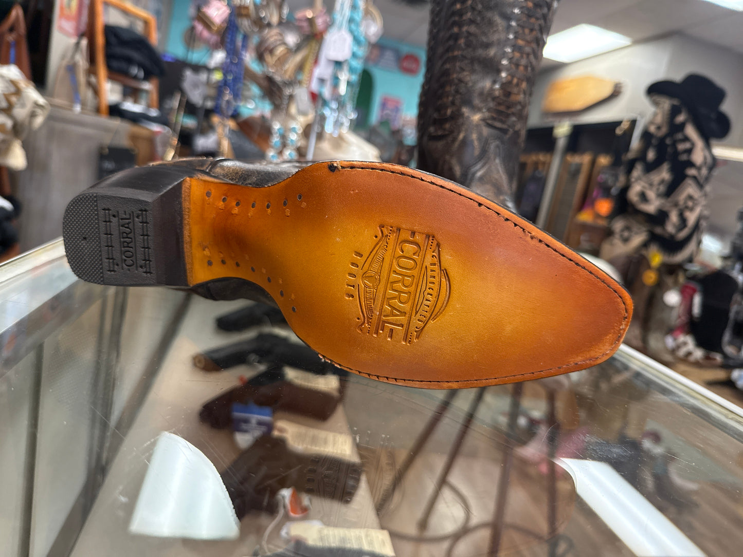 Close-up of a brown leather shoe sole with a brand logo, blurred store interior in the background