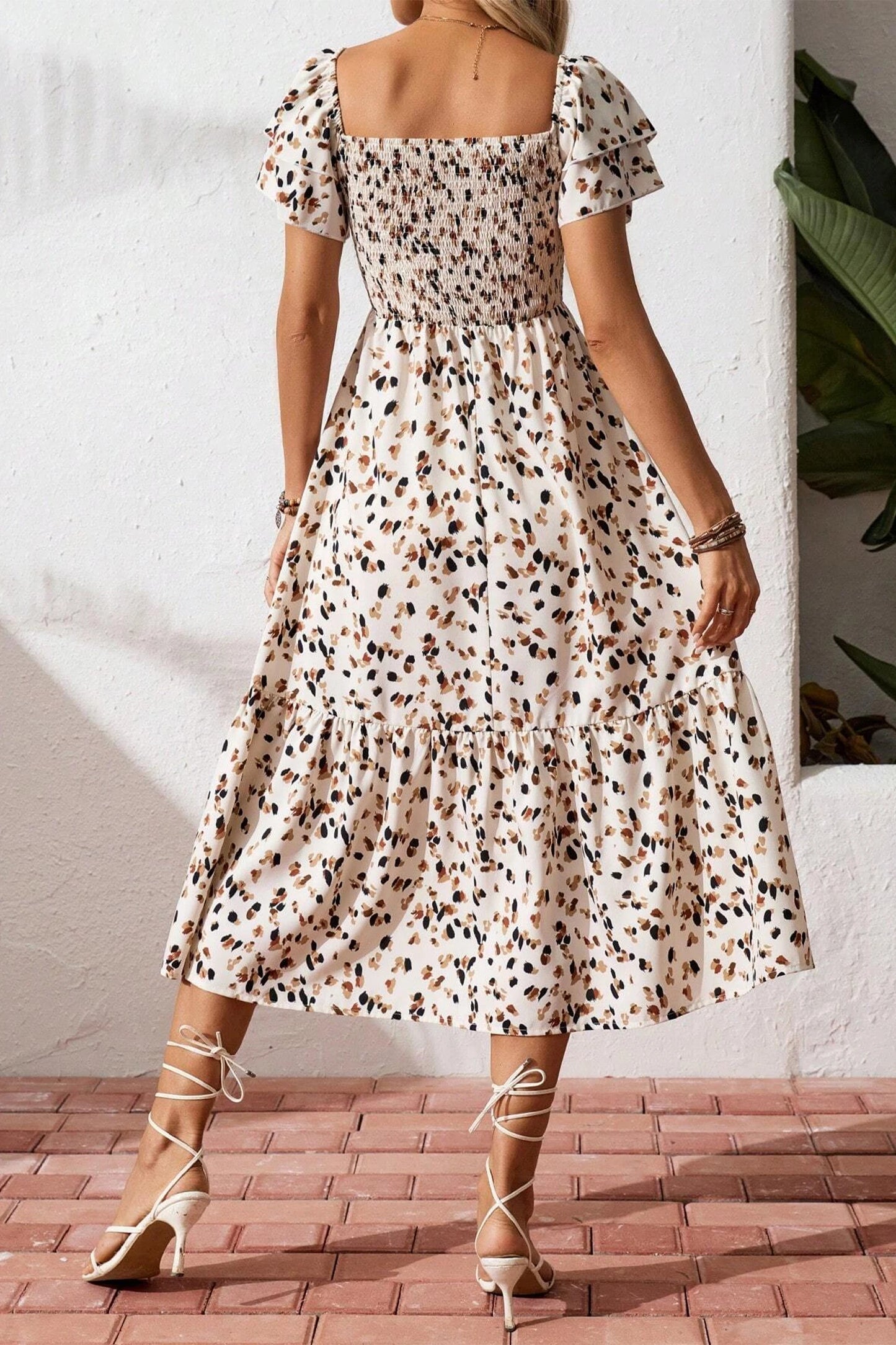 Woman wearing a patterned dress standing on a brick floor with a white wall background