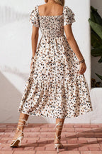 Woman wearing a patterned dress standing on a brick floor with a white wall background