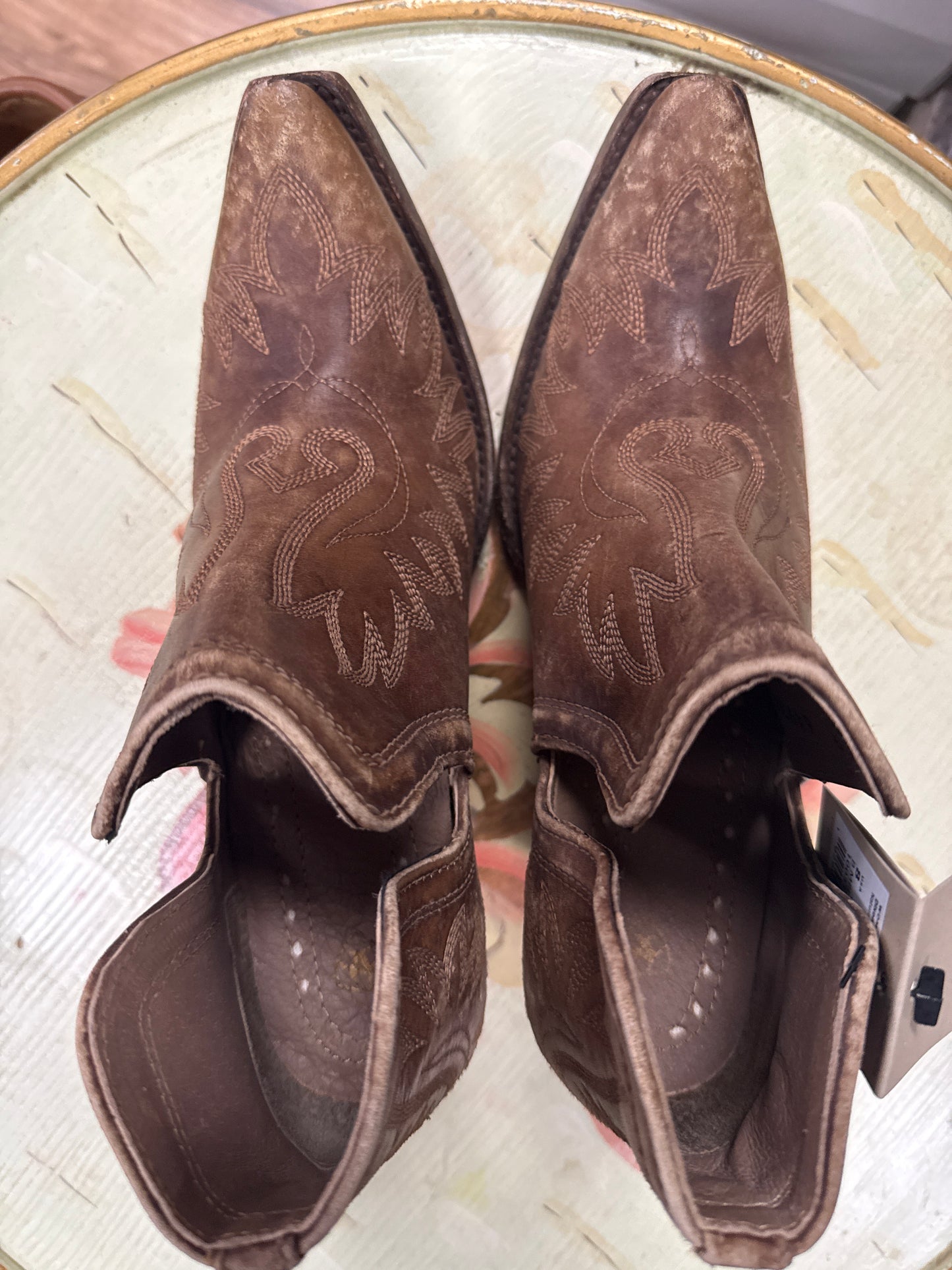 Pair of brown cowboy boots with embossed design on a light wooden surface.