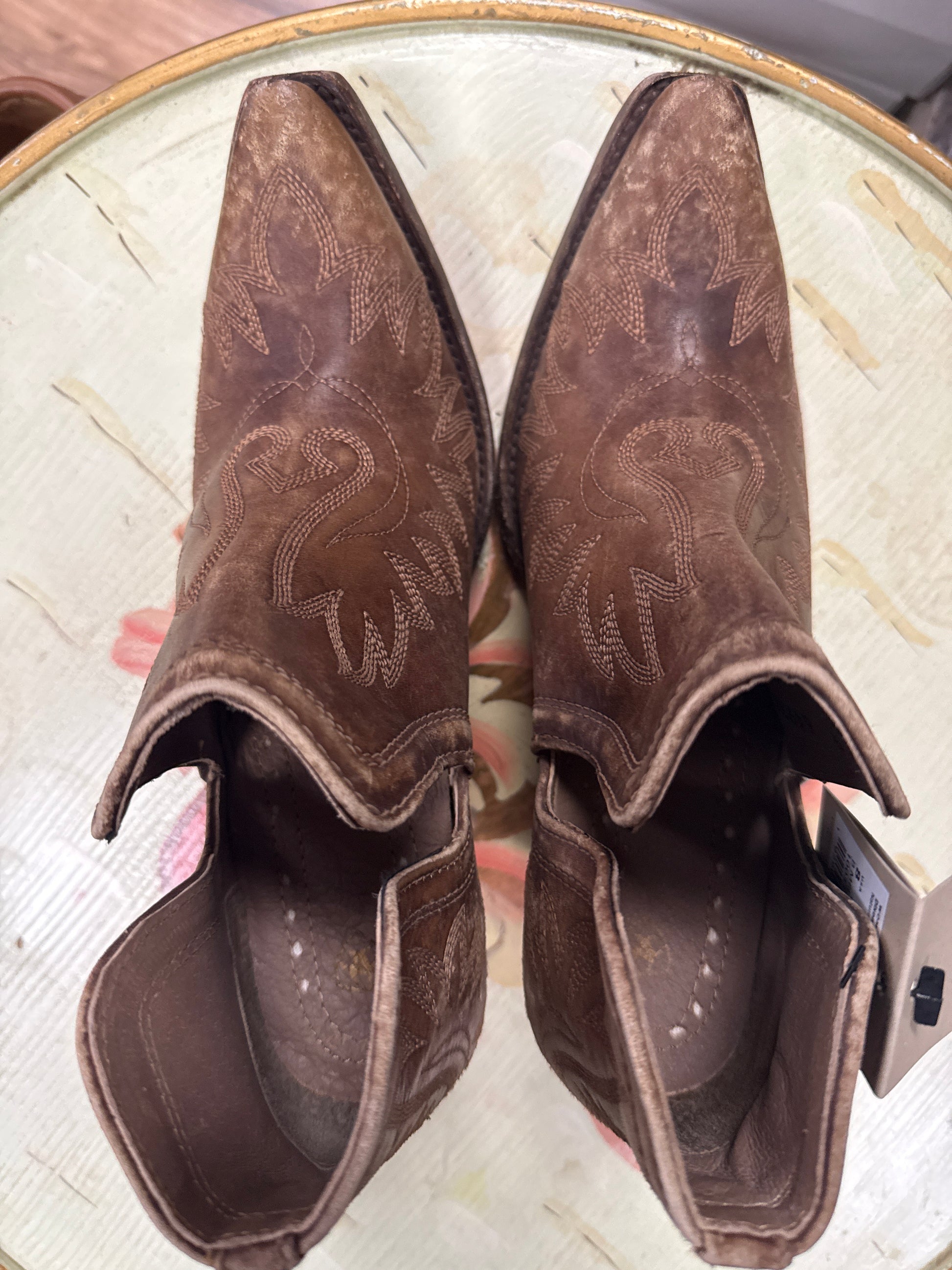 Pair of brown cowboy boots with embossed design on a light wooden surface.