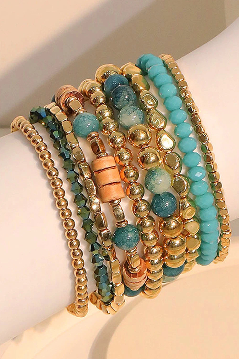 Stack of gold and turquoise beaded bracelets on a white arm.