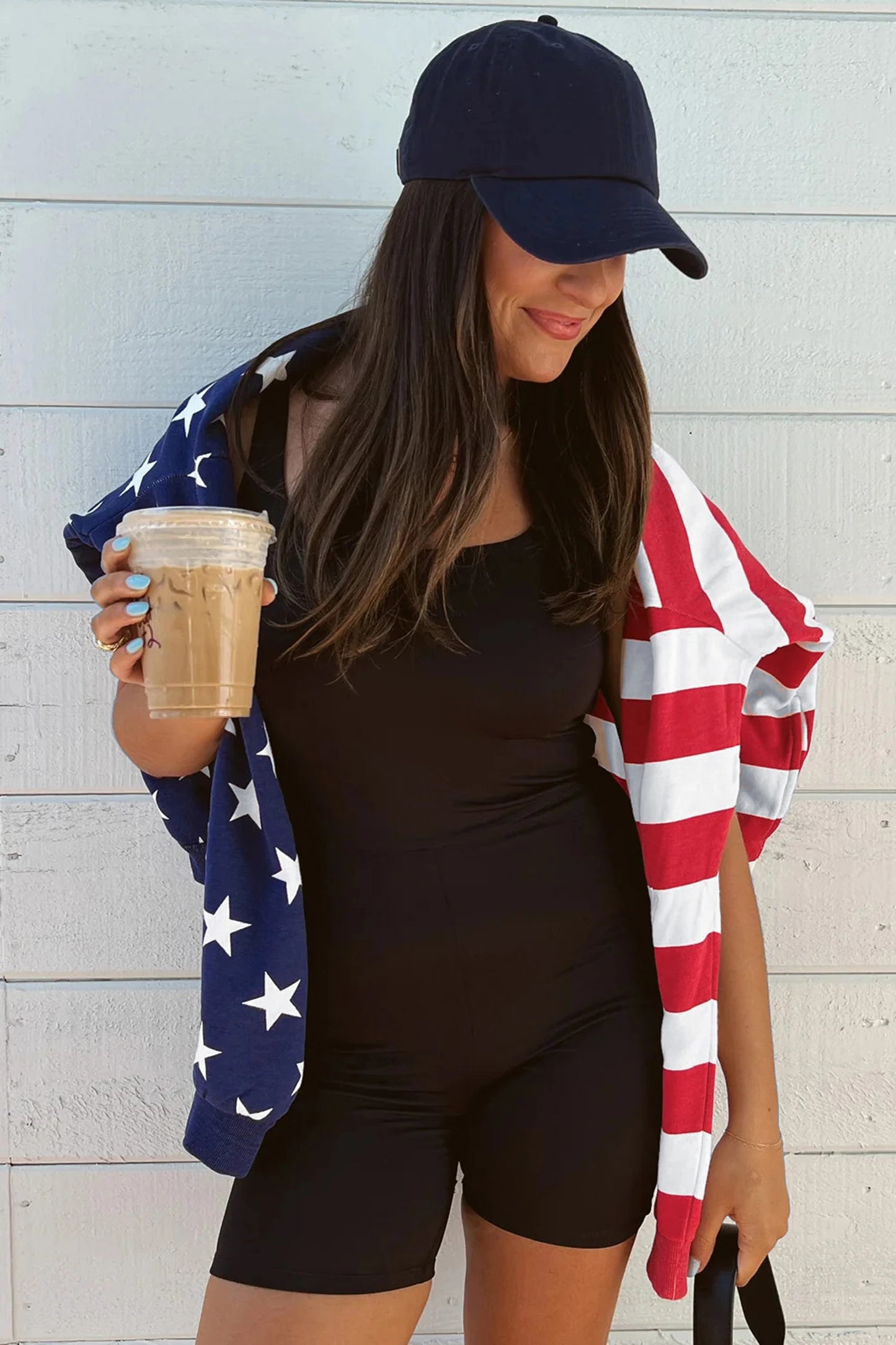 Woman holding a coffee cup with an American flag towel draped over her shoulders against a light wooden background
