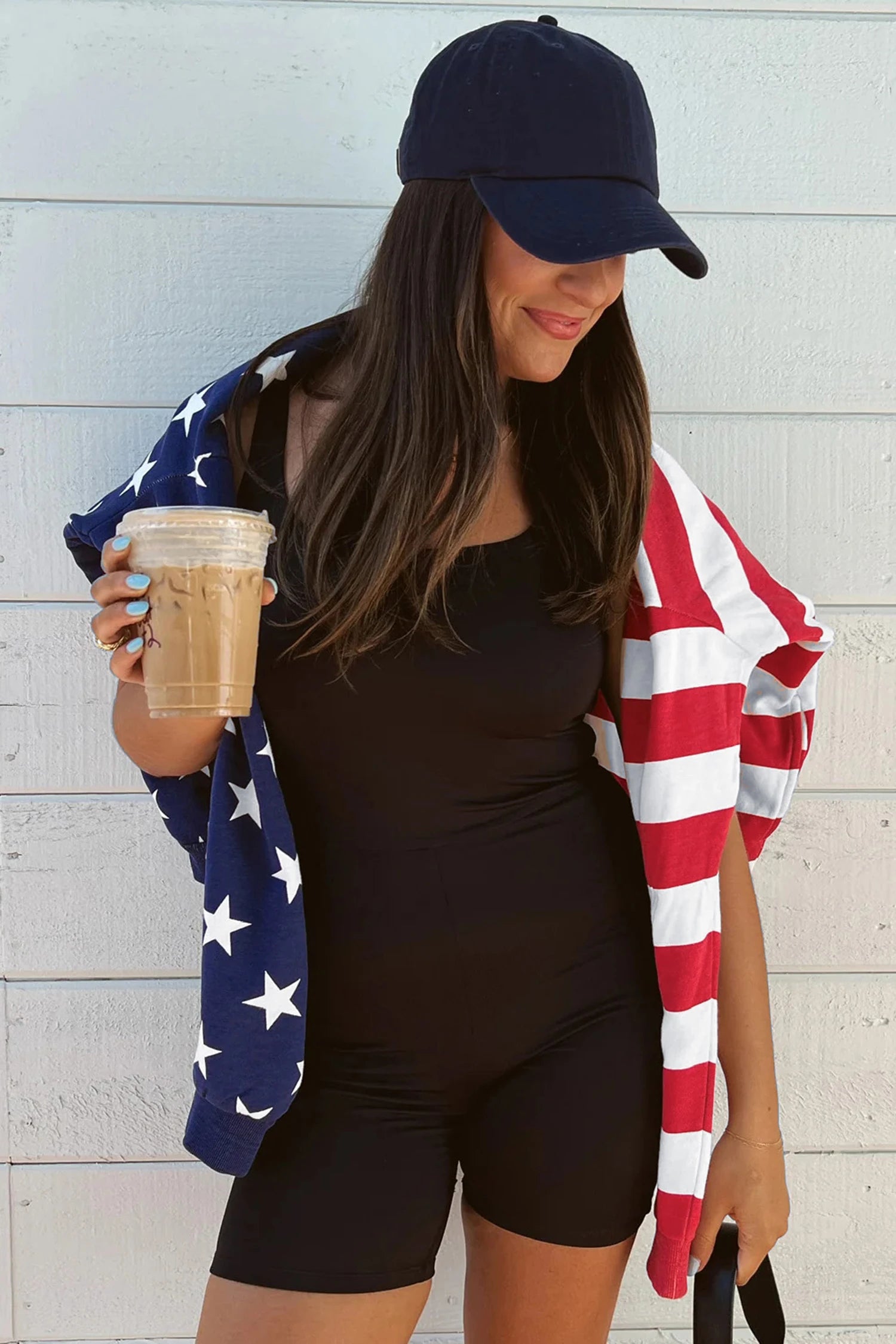 Woman holding a coffee cup with an American flag towel draped over her shoulders against a light wooden background