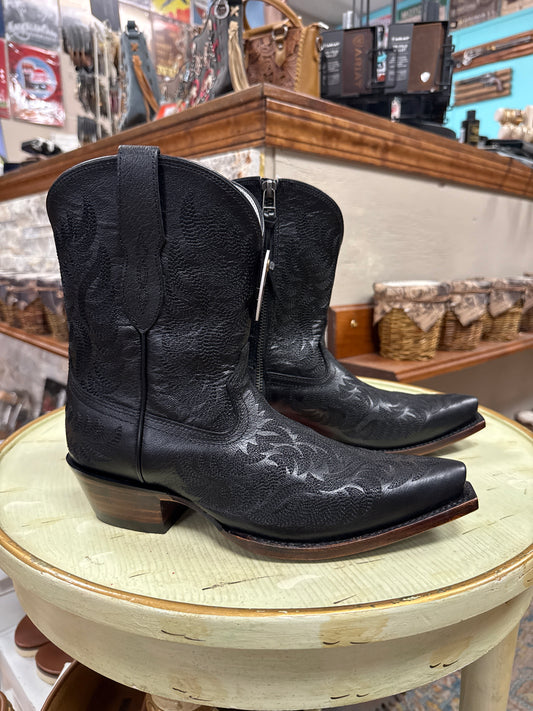 Black leather boot with decorative patterns on a round wooden surface.