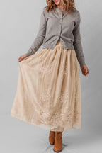Woman wearing a gray cardigan and beige lace skirt on a plain background