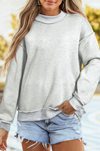 Person wearing a gray sweatshirt and denim shorts with a blurred outdoor background