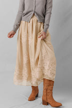 Person wearing a beige lace skirt with brown boots on a plain background