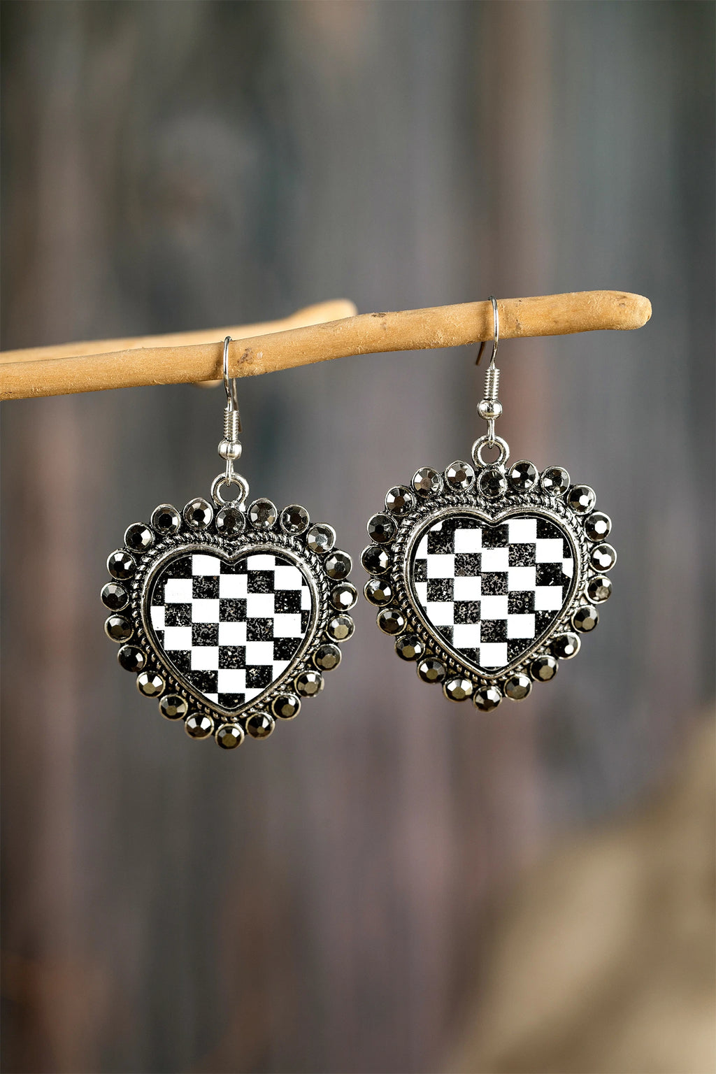 Heart-shaped earrings with black and white checkered design hanging on a branch.