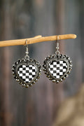 Heart-shaped earrings with black and white checkered design hanging on a branch.