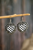 Heart-shaped earrings with black and white checkered design hanging on a branch.