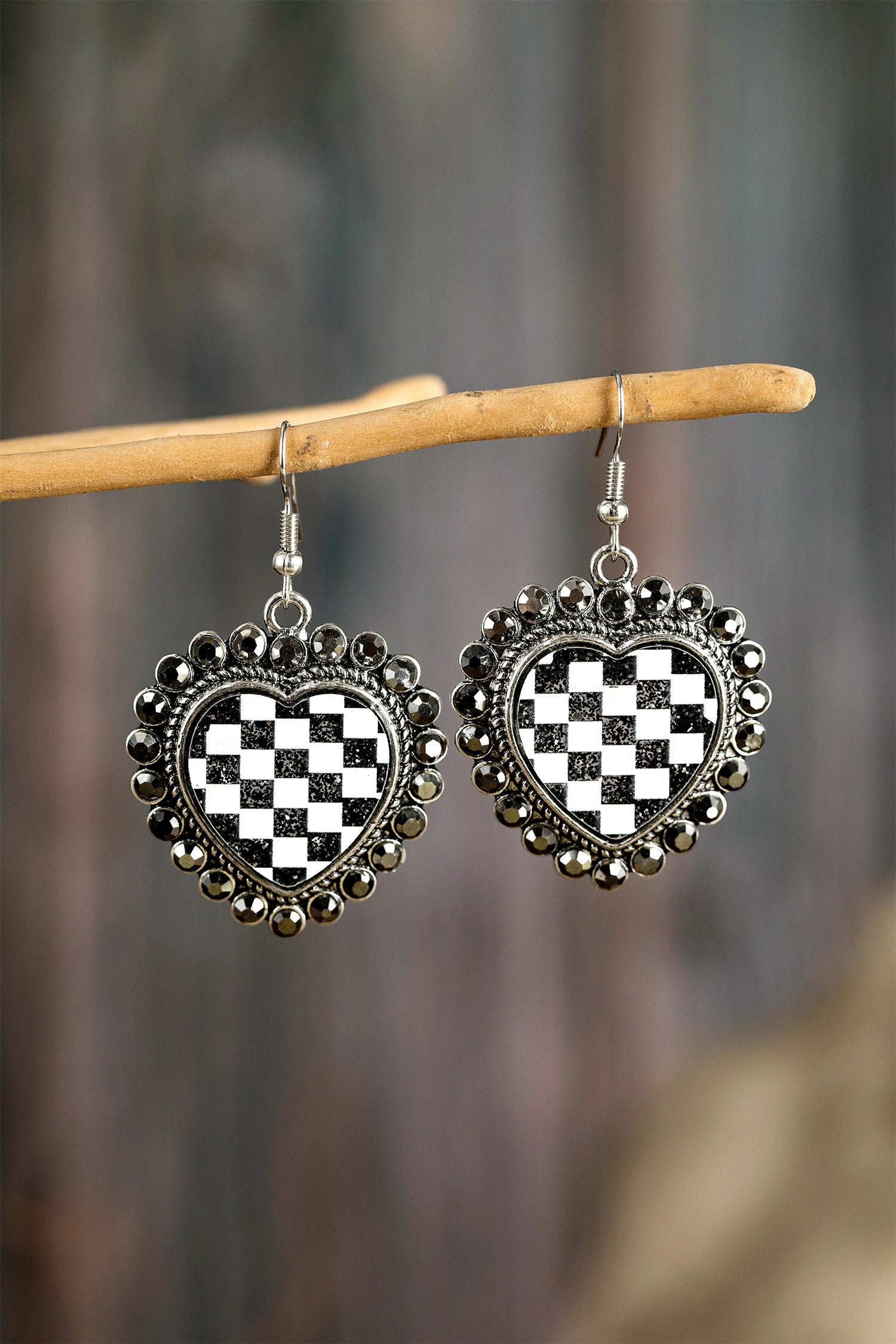 Heart-shaped earrings with black and white checkered design hanging on a branch.