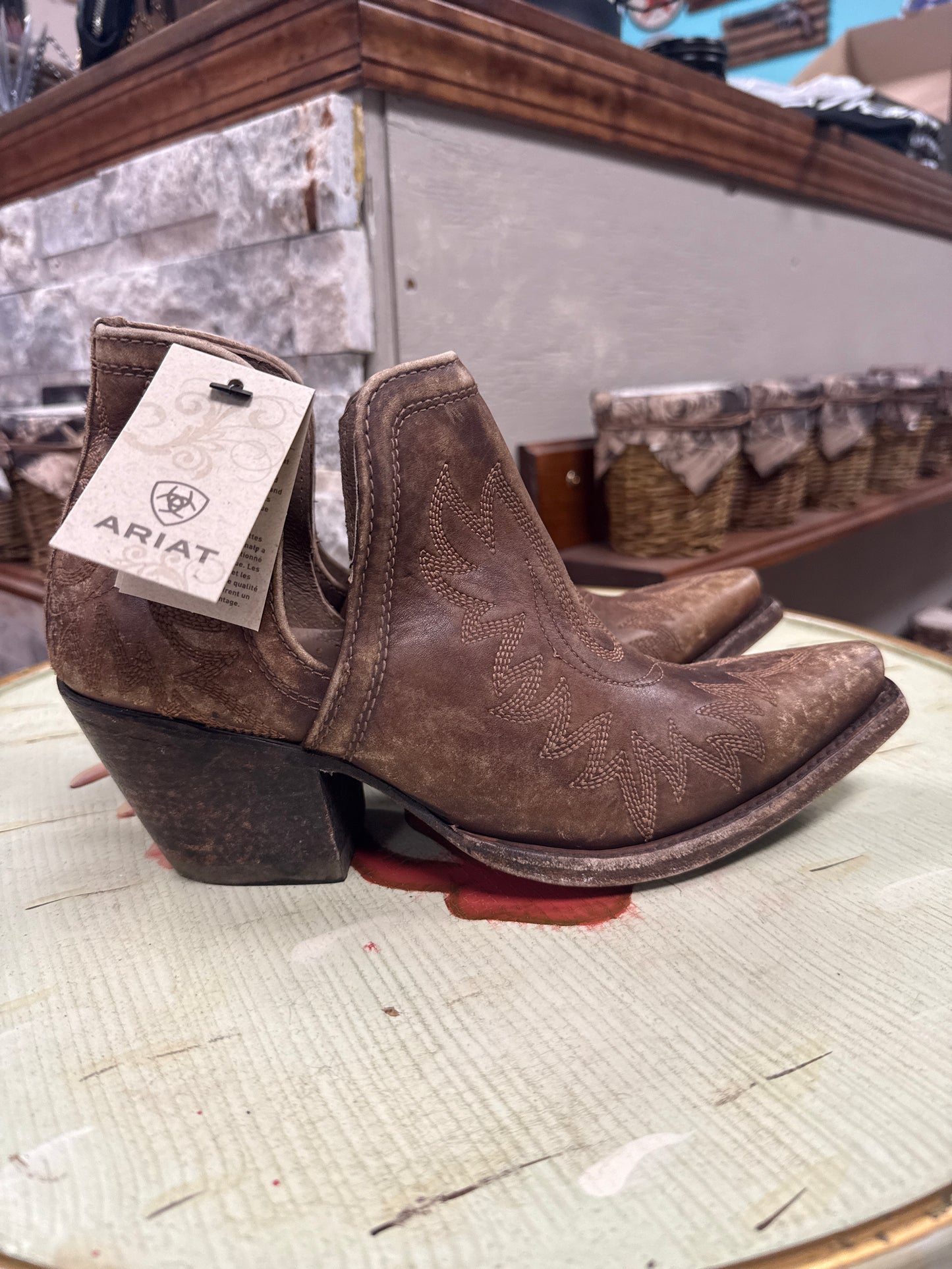 Brown cowboy boots with Ariat tag on a wooden surface