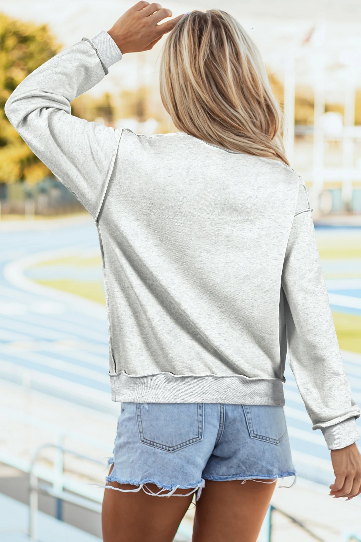 Person wearing a light gray sweatshirt and denim shorts with a blurred outdoor background
