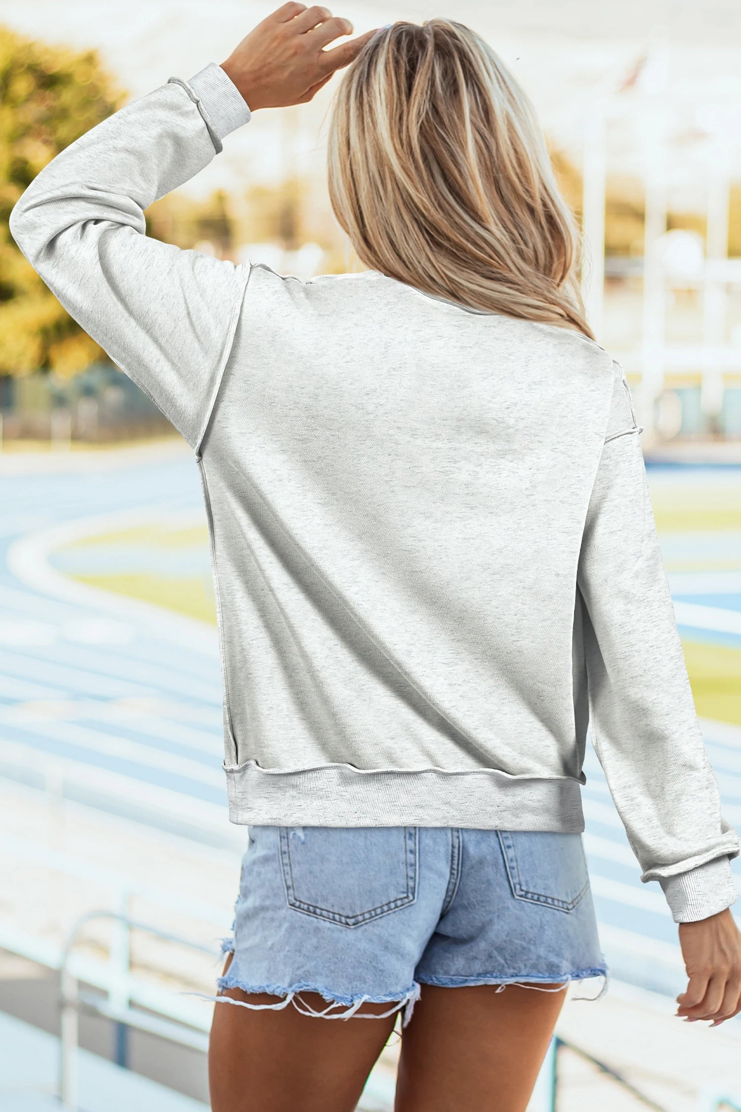Person wearing a light gray sweatshirt and denim shorts with a blurred outdoor background