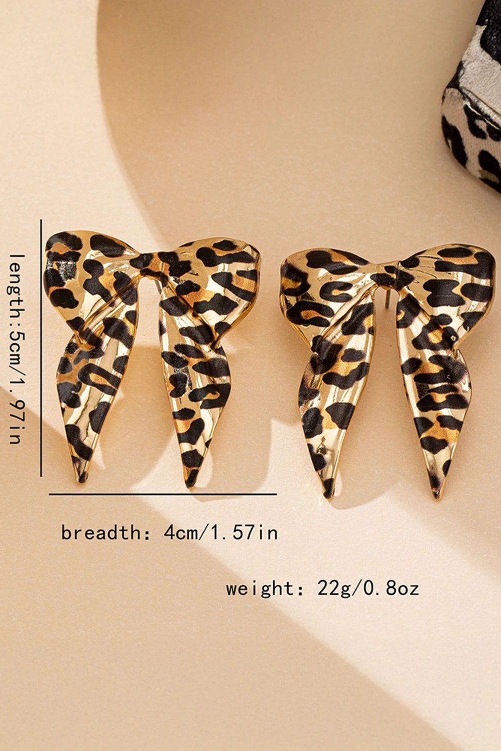 Leopard print butterfly-shaped earrings with measurements on a beige background