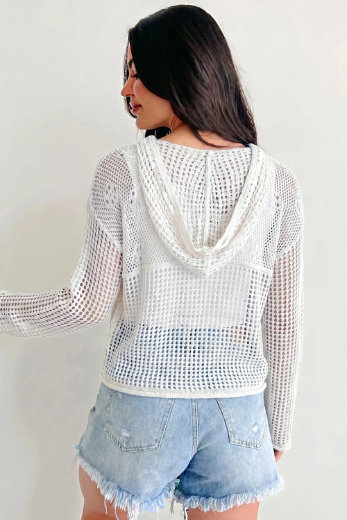 Woman wearing a white crochet top and denim shorts against a plain background