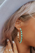 Close-up of a person wearing turquoise hoop earrings with a neutral background