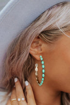Close-up of a person wearing turquoise hoop earrings with a neutral background