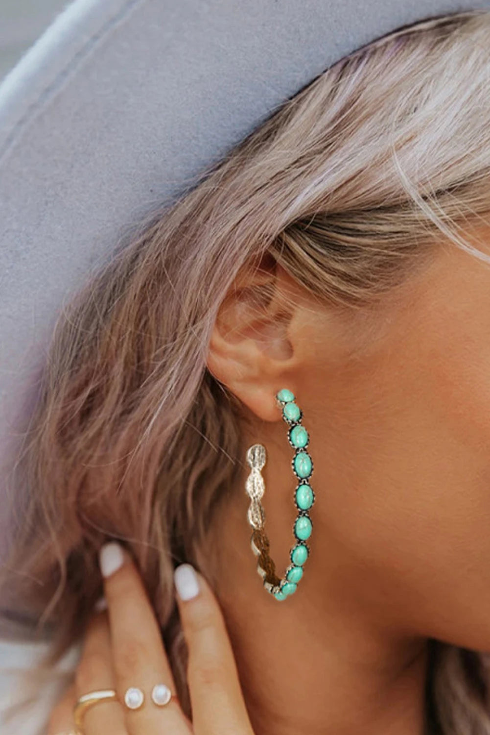 Close-up of a person wearing turquoise hoop earrings with a neutral background