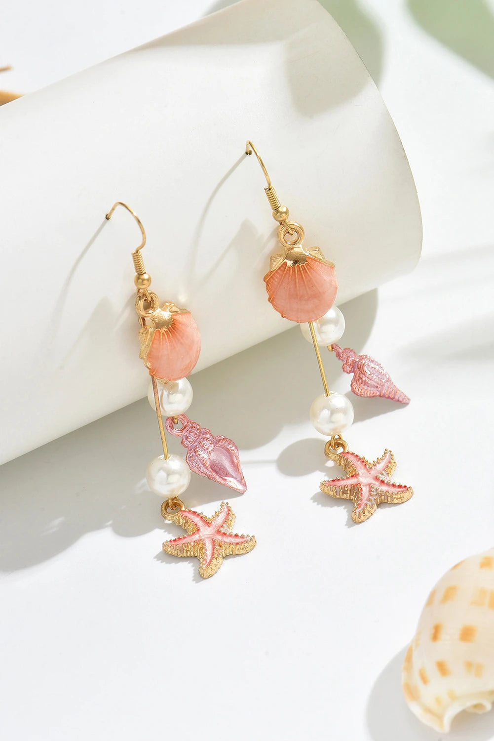 Pair of earrings with starfish and shell charms on a white surface