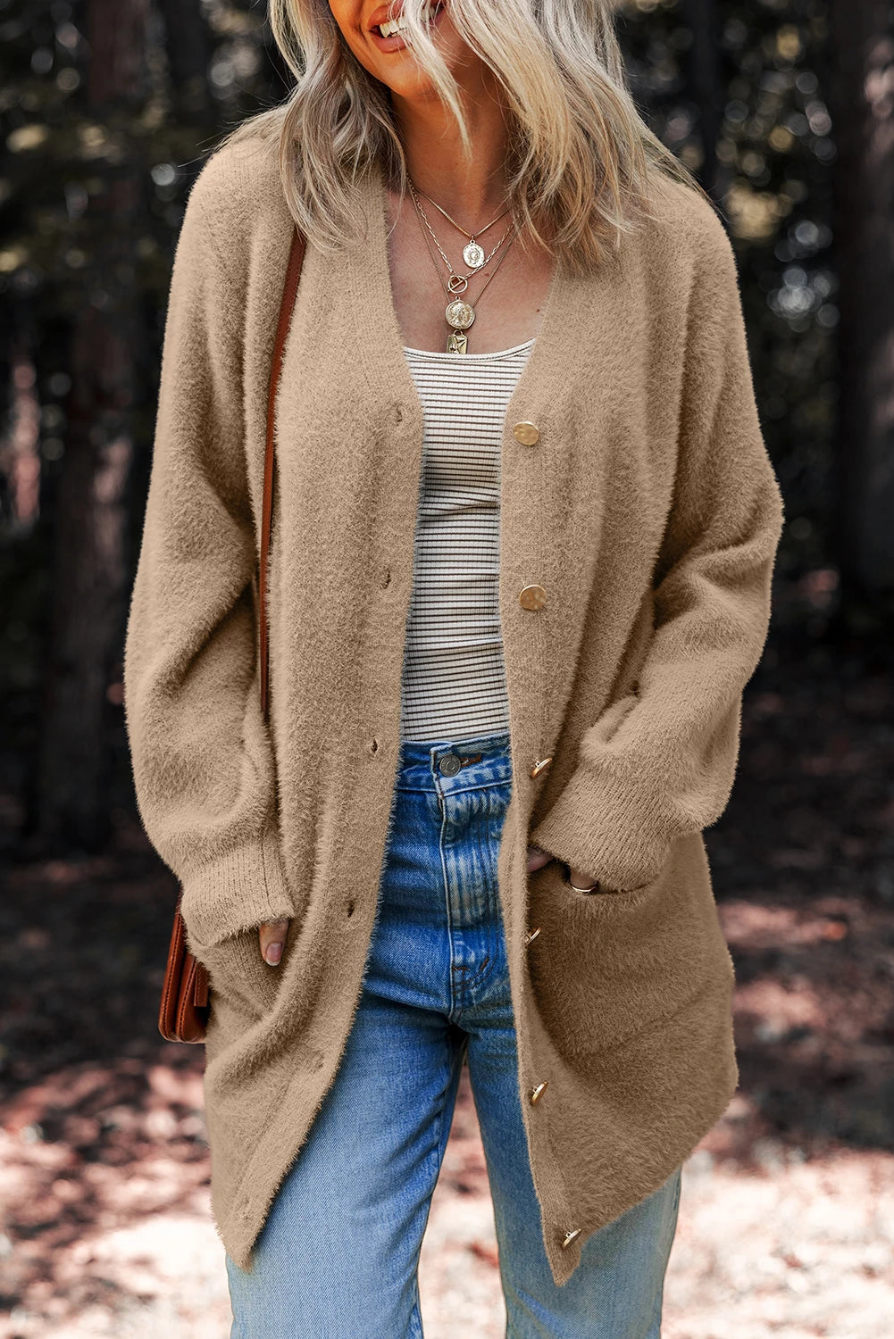 Woman wearing a beige cardigan over a striped shirt and blue jeans, standing outdoors.