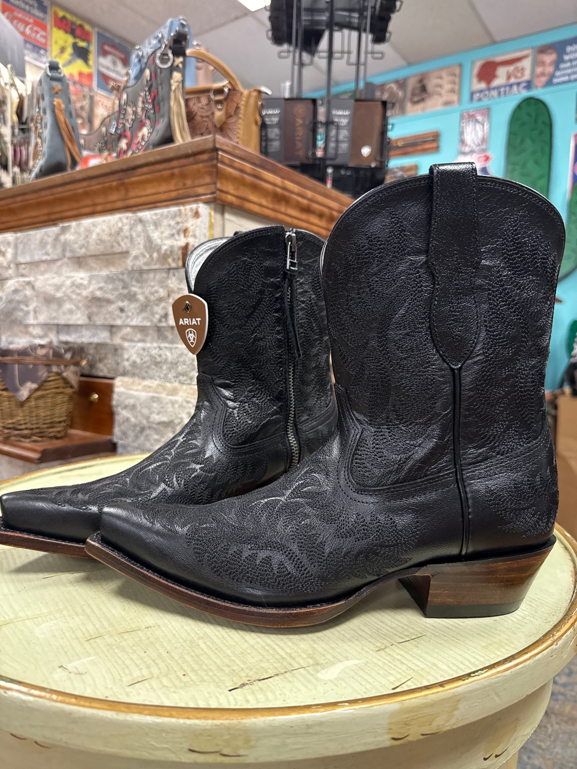 Black leather cowboy boots with brown soles on a wooden surface.