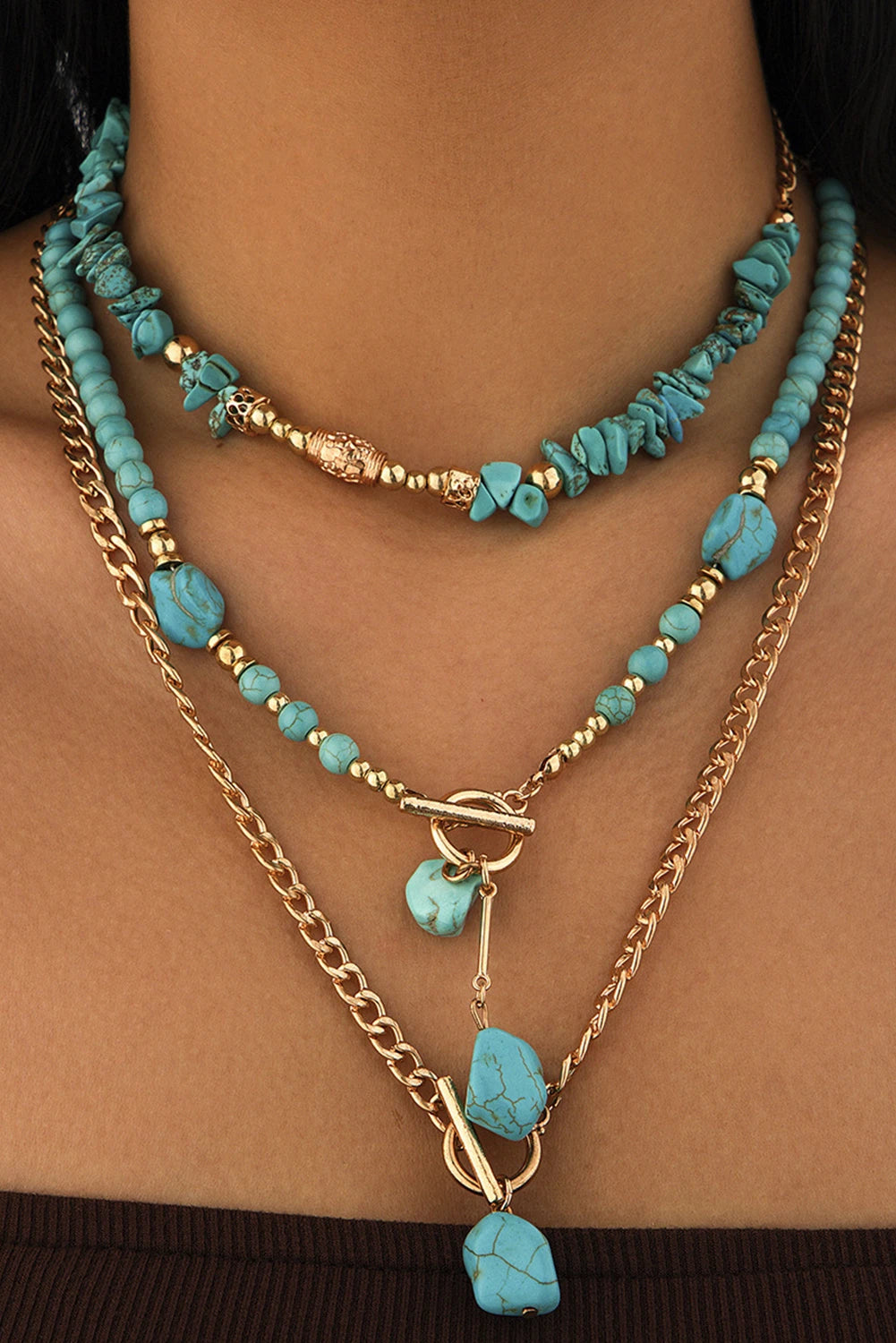 Layered necklaces with turquoise beads and gold chains on a person's neck.