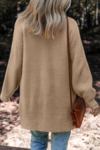 Person wearing a beige sweater holding a brown bag outdoors.