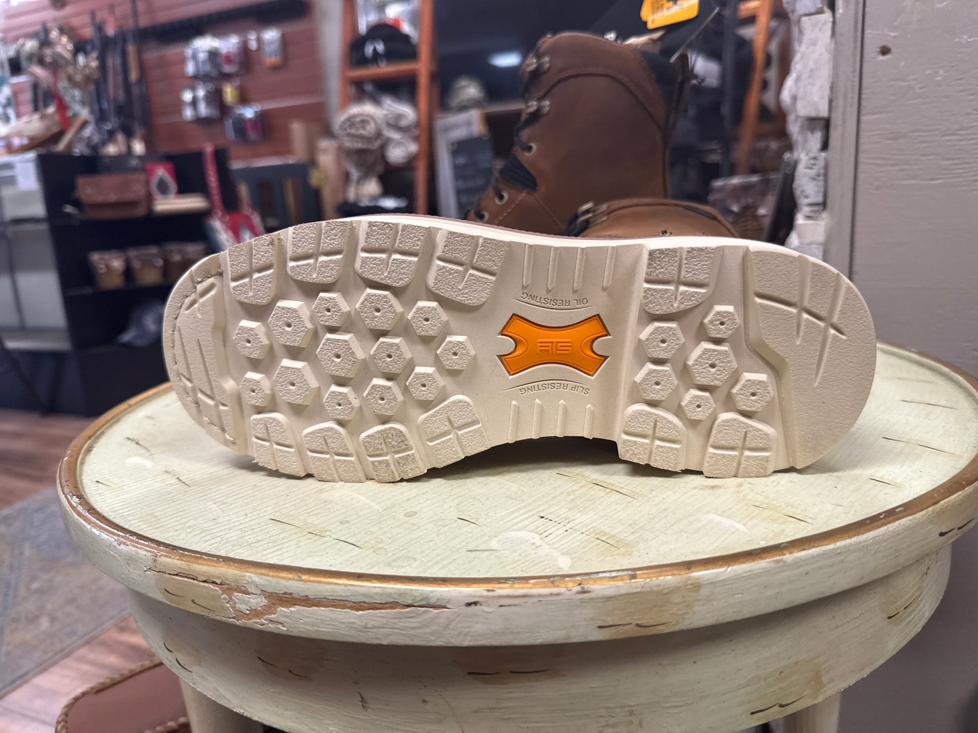 Brown boot with a visible brand logo on a light green stool in a store setting