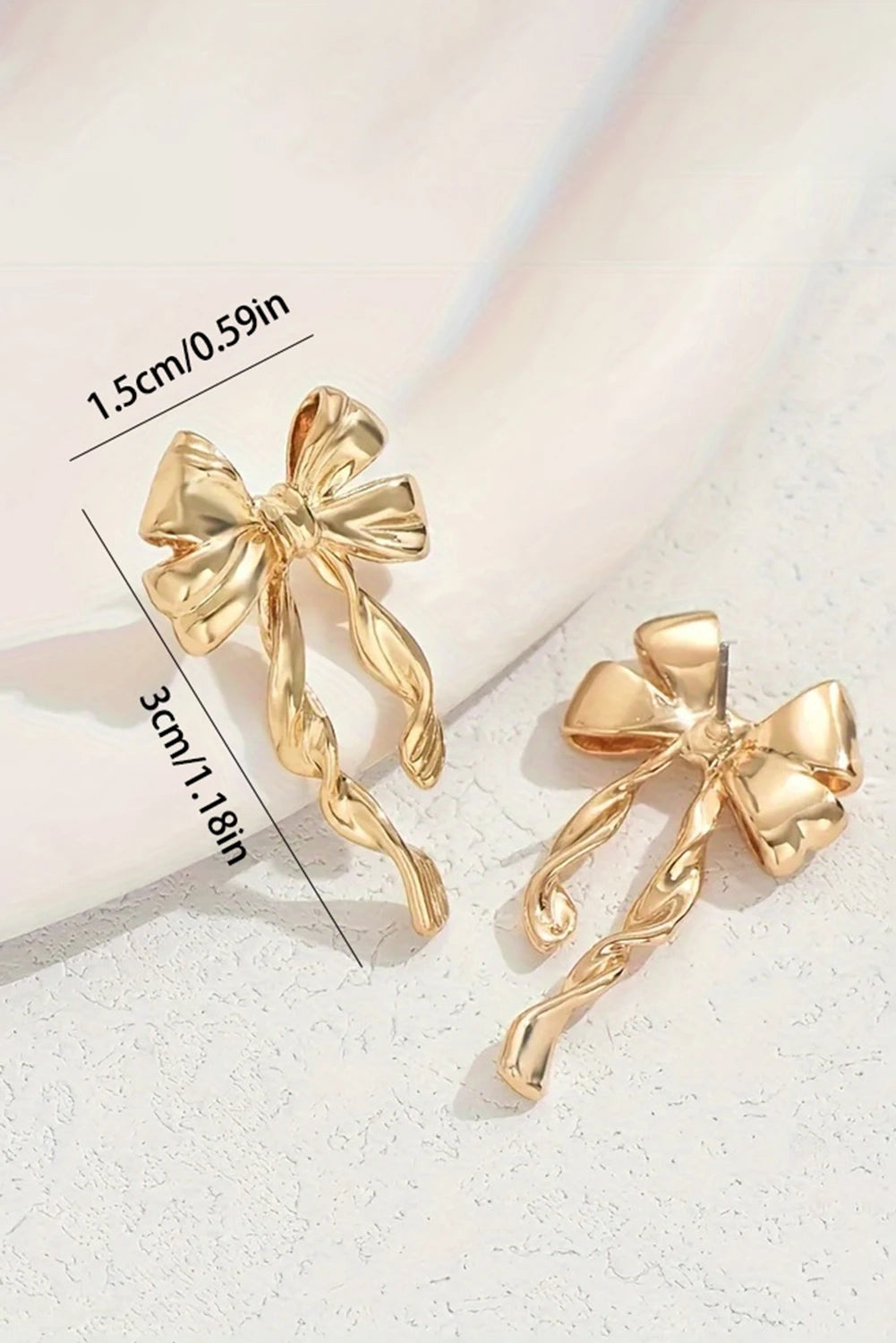 Gold bow-shaped earrings with measurements on a light background