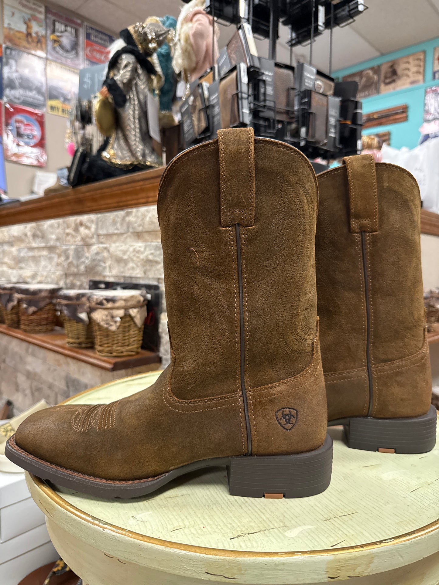 Brown suede boots on a circular display stand in a store setting.