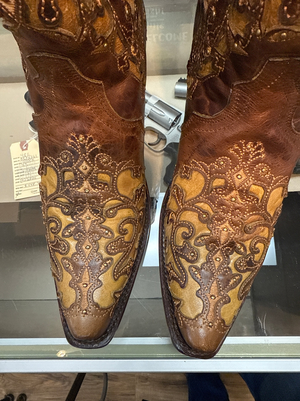 Pair of brown leather boots with intricate gold embroidery on a glass surface.