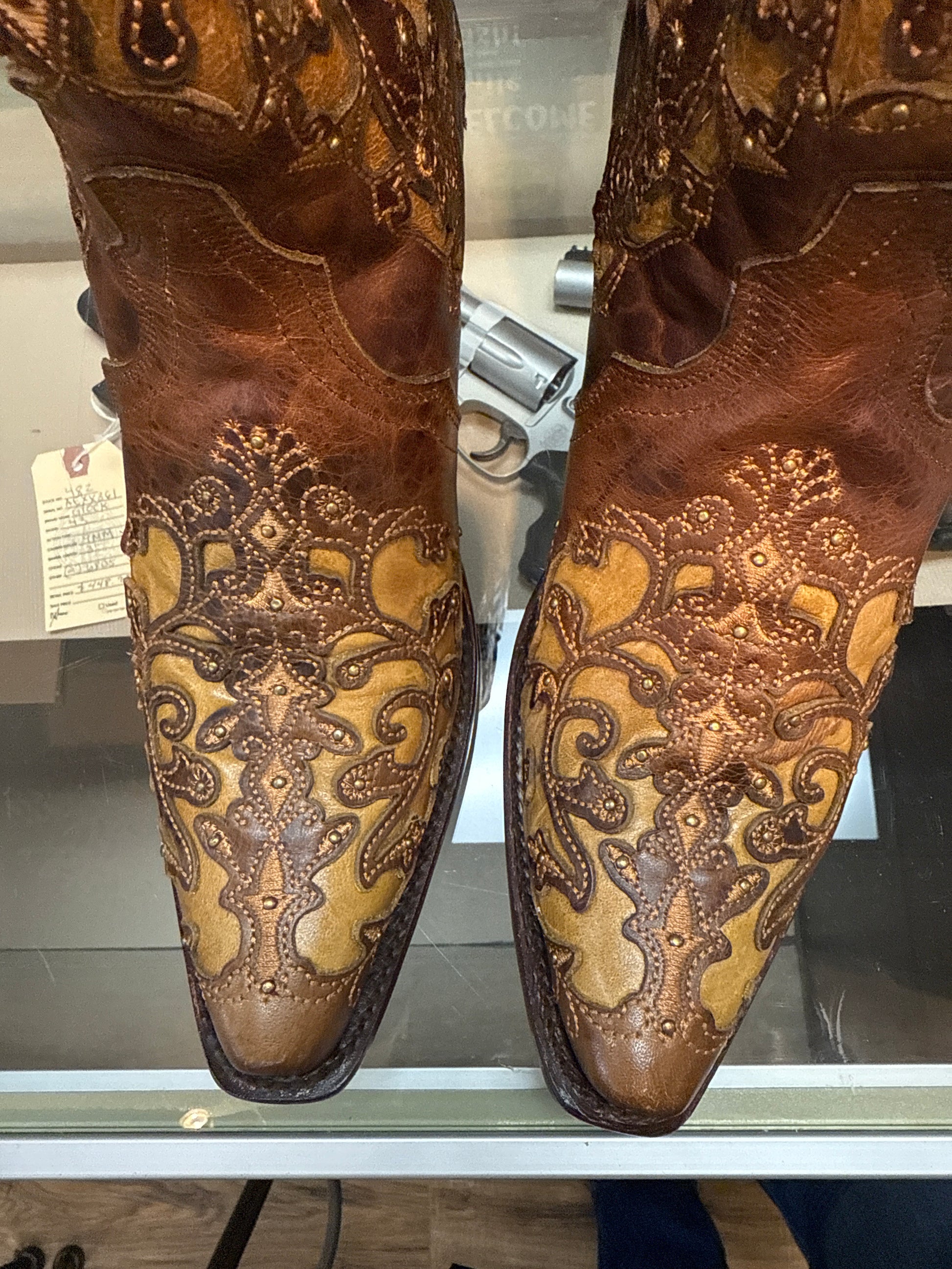Pair of brown leather boots with intricate gold embroidery on a glass surface.