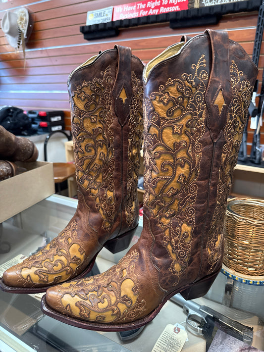 Pair of intricately designed brown leather boots with gold embroidery on a blurred indoor background.