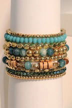 Stack of turquoise and gold beaded bracelets on a white stand.