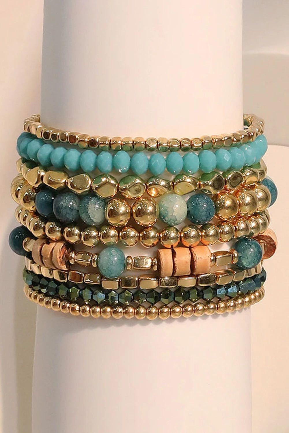 Stack of turquoise and gold beaded bracelets on a white stand.
